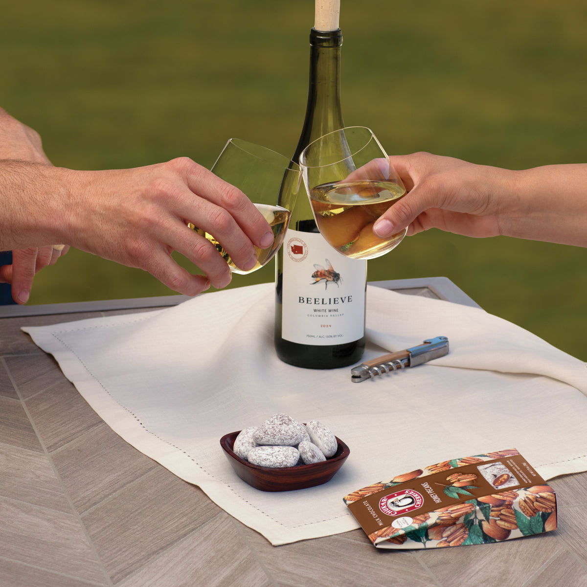 Beelieve chardonnay in bottle and glasses is shown being toasted and with milk chocolate honey pecans