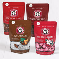 Closed bags of milk chocolate classic cherries, dark chocolate classic cherries, milk chocolate honey pecans, and dark and white chocolate cherry blossoms.