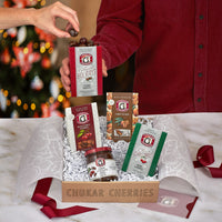 Open holiday joy gift box shown with person holding open box of happy holidays cherry quartet and complimentary greeting card in velum envelope.