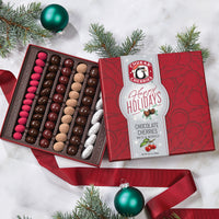 Open happy holidays original chocolate assortment gift box showing whole white chocolate raspberry truffles, dark chocolate cabernet cherries, milk chocolate cherry bings and truffle cherries, classic dark chocolate cherries, and milk chocolate honey peca