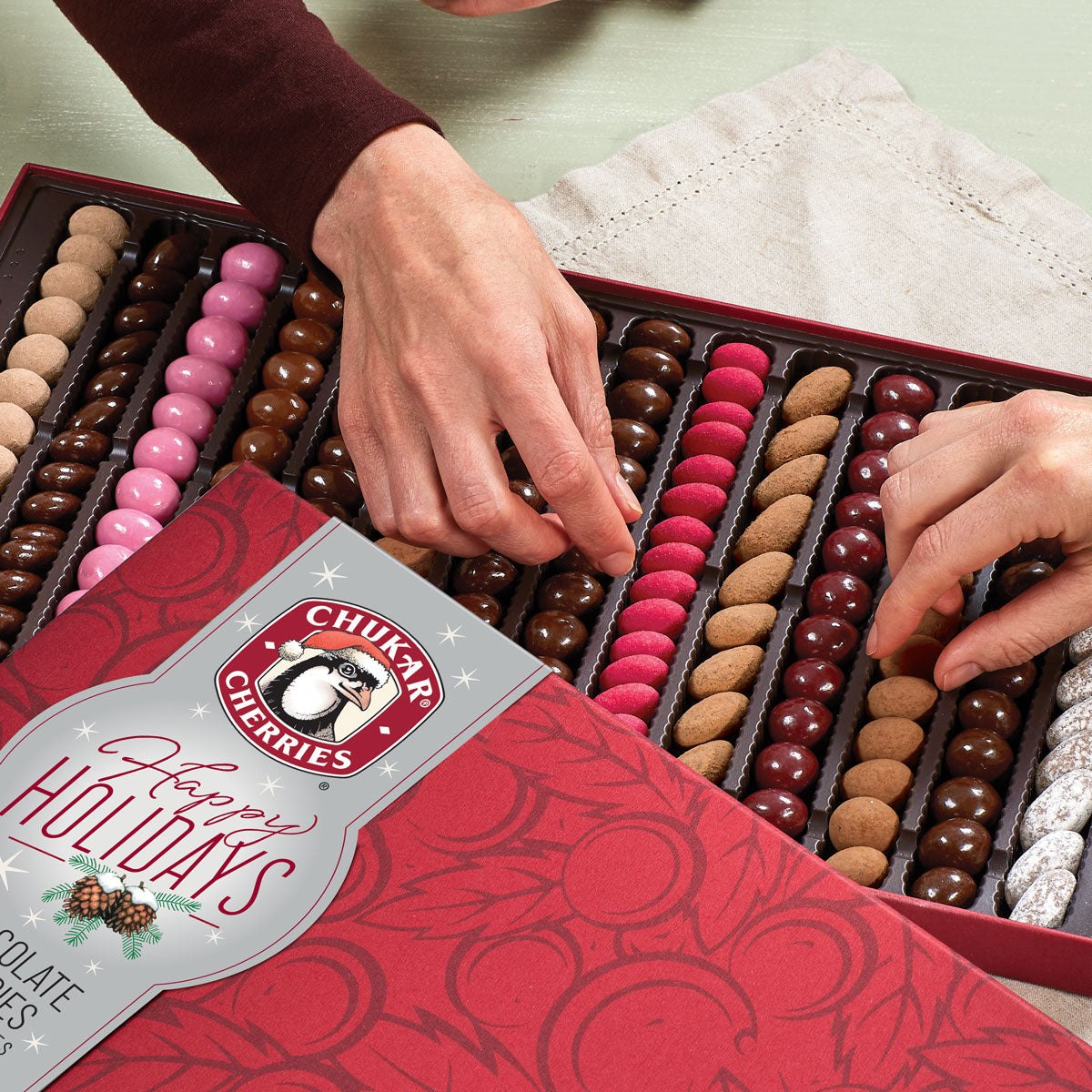 Close up view of holiday sumptuous chocolate assortment with hands picking chocolates out of box