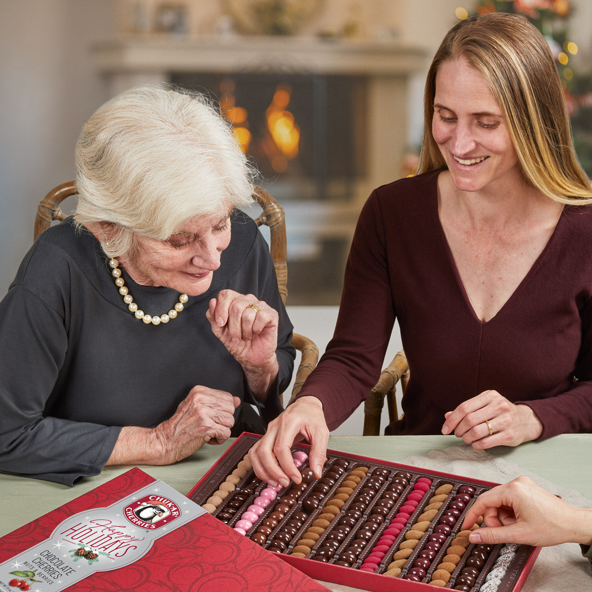 Two smiling women picking chocolate covered cherries out of happy holidays sumptuous assortment 
