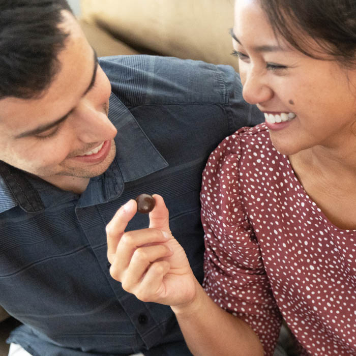 Two people smiling, with one holding a chocolate covered cherry.