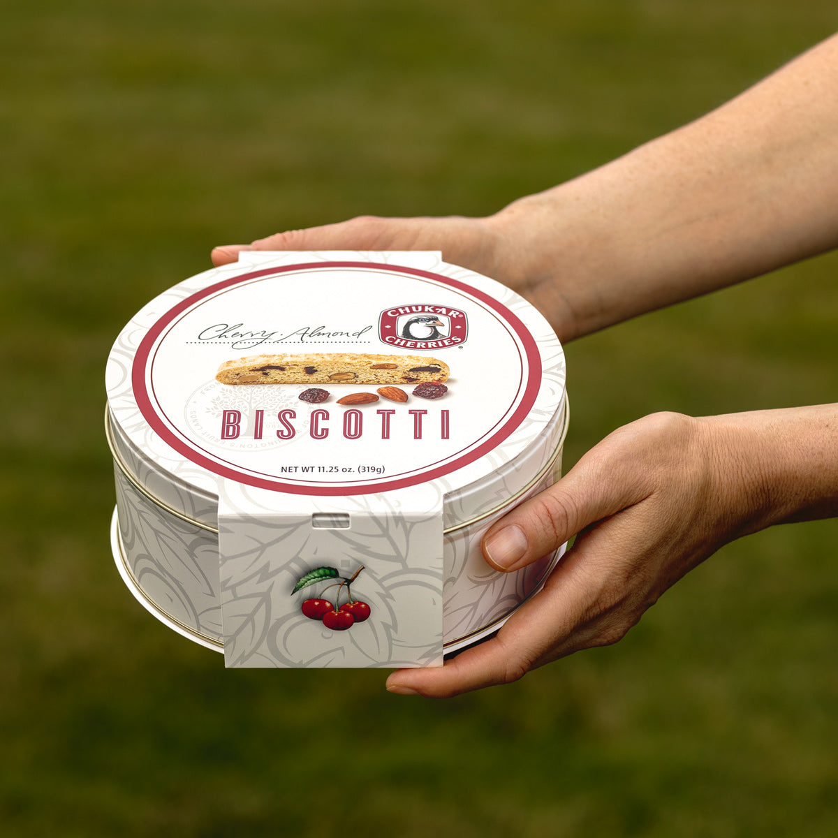 Closed cream gift tin with biscotti and cherries pictured on band 
