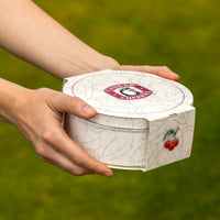 Closed cream colored gift tin in the hands of a gift giver