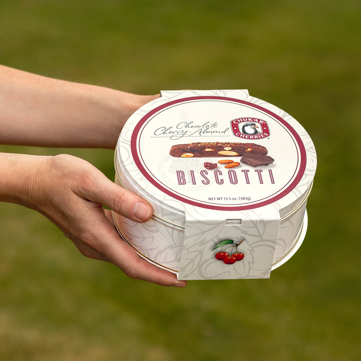Closed cream gift tin with biscotti and cherries pictured on band