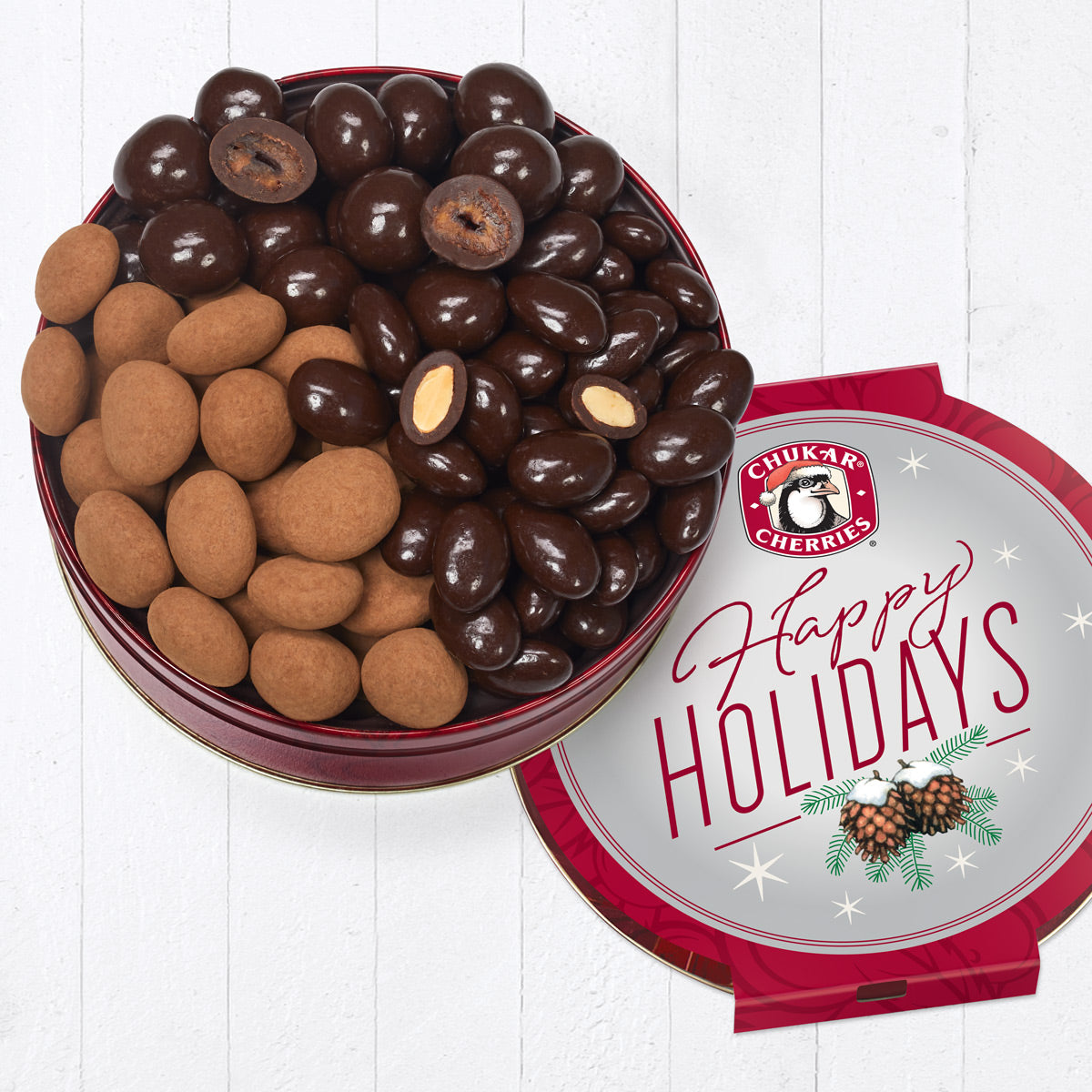 Open happy holidays dark chocolate tin showing whole and cut dark chocolate classic cherries, ultra dark chocolate vanilla almonds, and ultra dark chocolate black forest cherries.