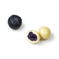 Fresh blueberry beside cut white chocolate blueberry showing dried blueberry center and thick white chocolate coating.