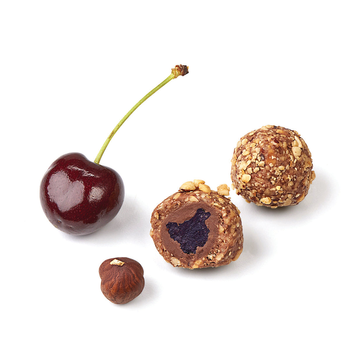 Fresh bing cherry and hazelnut next to cut chocolate cherry showing dried cherry center thick chocolate coating and crushed hazelnut finish