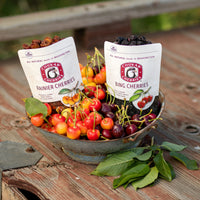 Open bags of bing and rainier cherries in a bowl with fresh cherries