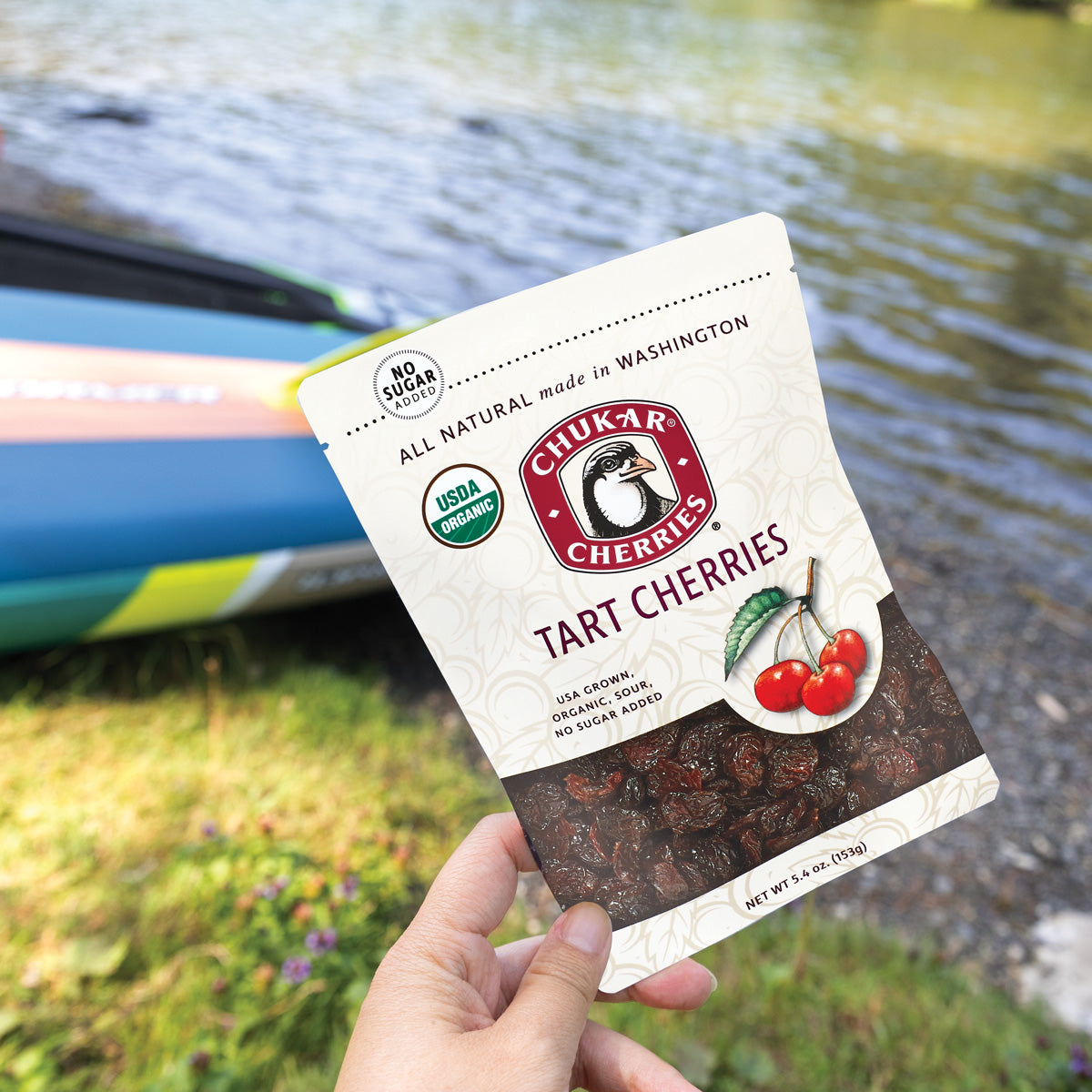 Hand holding organic tart cherries bag with river in the background
