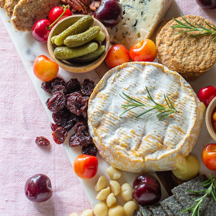 Charcuterie board with dried organic tart cherries, warm camembert, pickles, crackers, and fresh cherries