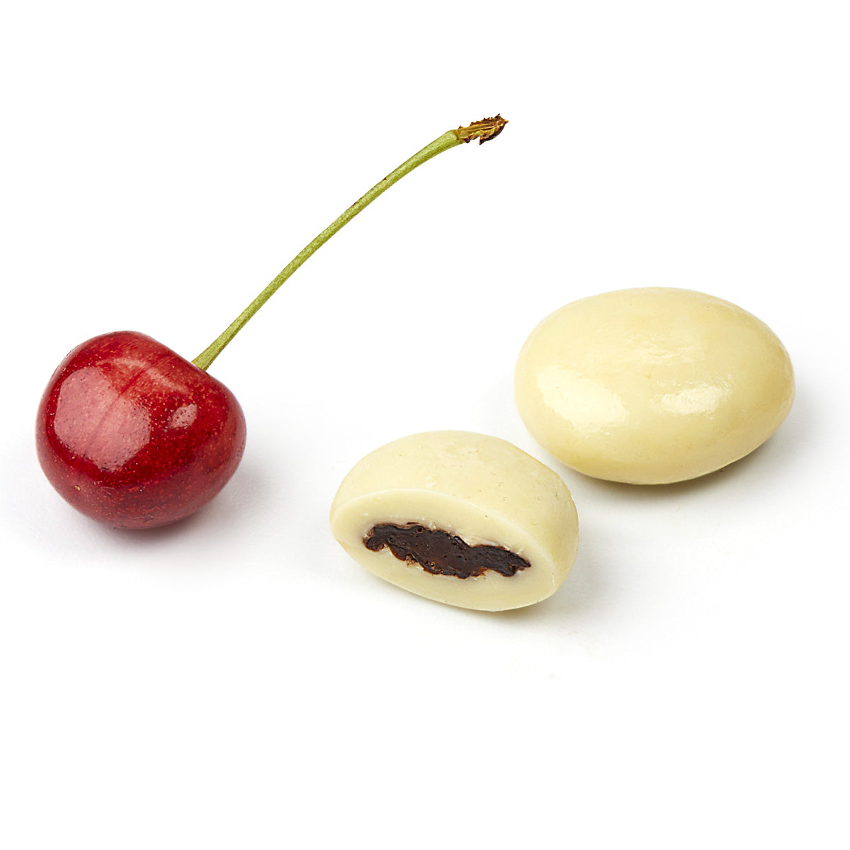 Close up of Christmas Snow Cherries with dried tart cherries and white chocolate. One piece is cut to show whole tart cherry center.  A fresh tart cherry sits next to the chocolate pieces.