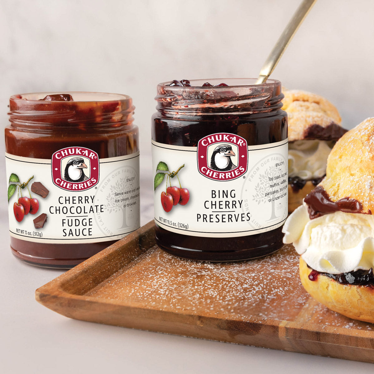 Open jars of bing cherry preserves and cherry chocolate fudge sauce next to cream puffs