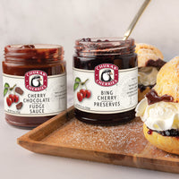Open jars of bing cherry preserves and cherry chocolate fudge sauce next to cream puffs