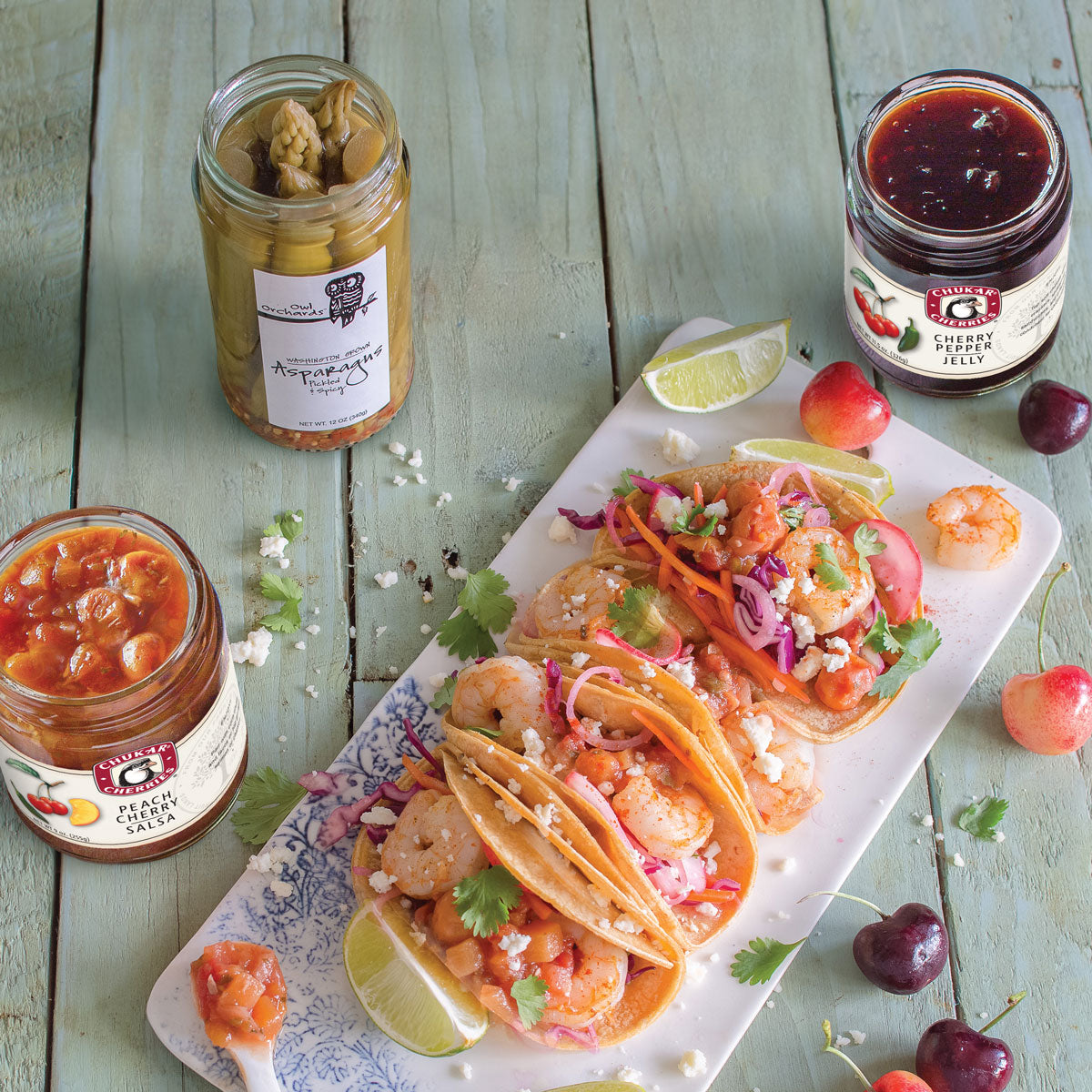 Open jars of peach cherry salsa, pickled asparagus, and cherry pepper jelly next to shrimp fajitas