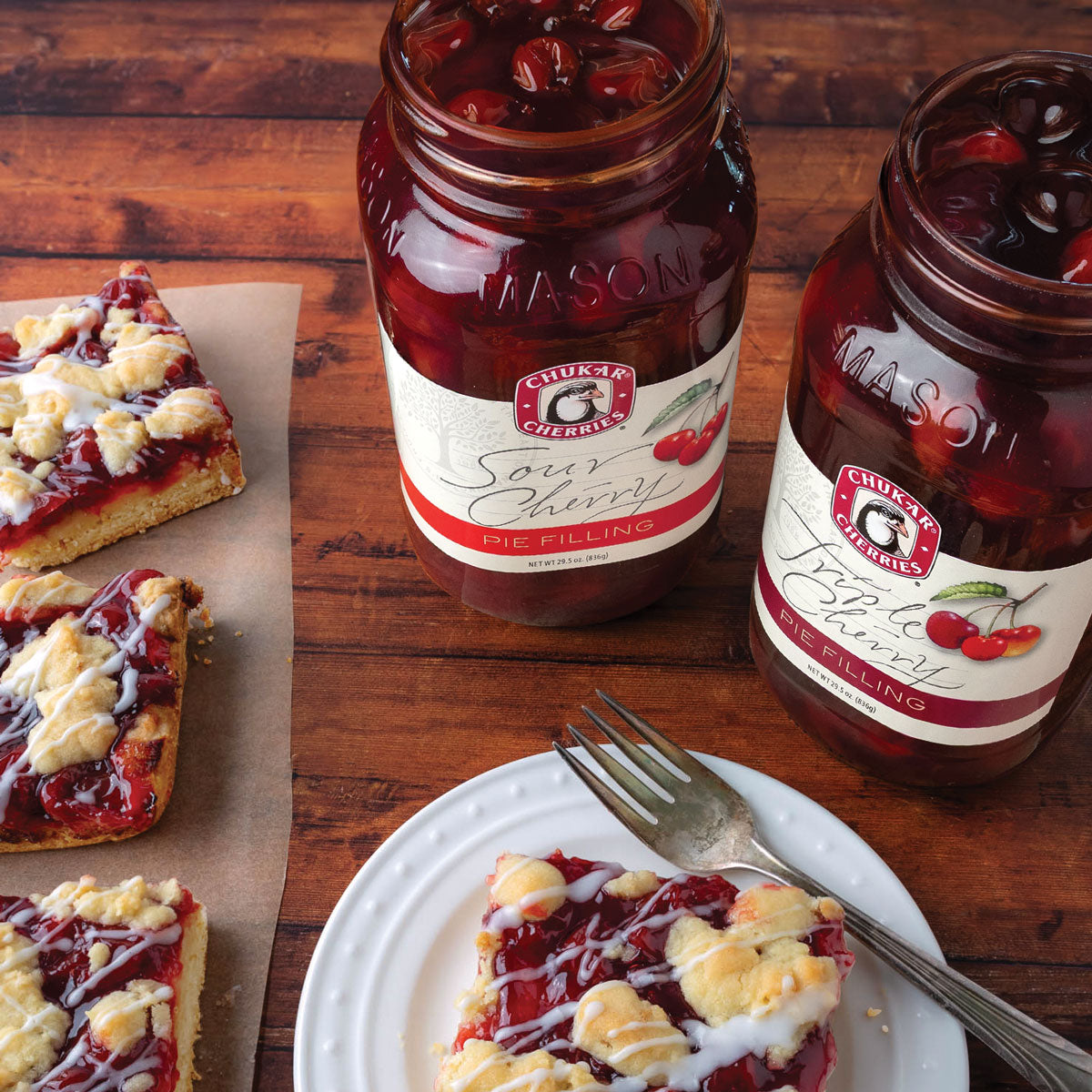 Open jars of sour and triple cherry pie filling next to cherry pie bars