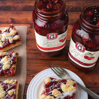 Open jars of sour and triple cherry pie filling next to cherry pie bars
