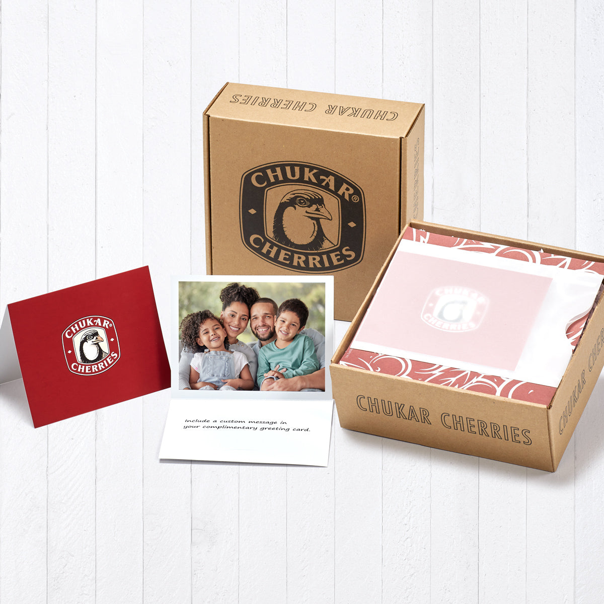 Three views of complimentary gift card shown; first view is of the front, second view is open with custom image and message, and the third view is in a vellum envelope placed at the top of the holiday classic gift box on the decorative inner wrapping.  